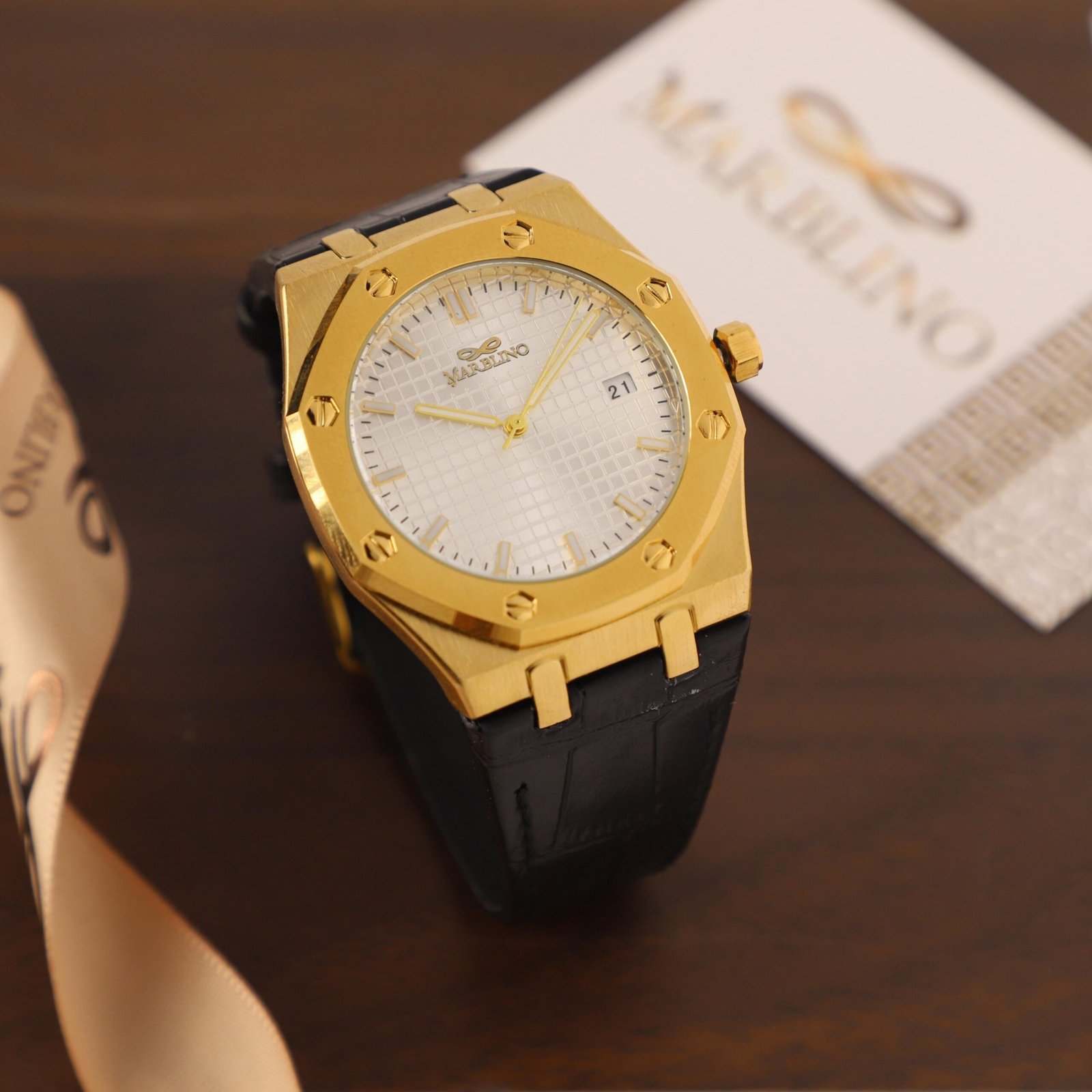 ​ساعة ماربلينو الذهبية ذات الميناء المنقوش والحزام الجلدي الأسود.