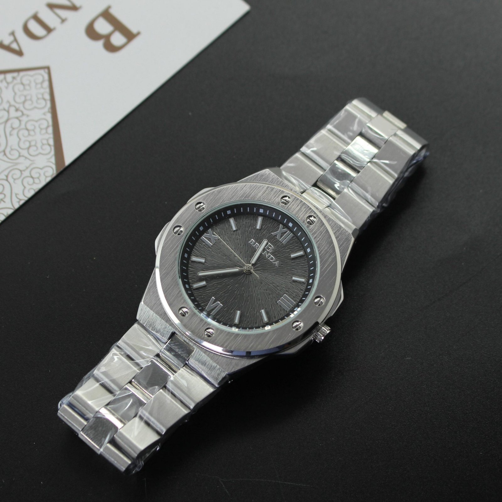 ساعة يد "BRENDA" رجالية/للجنسين معدنية فضية بتصميم رياضي فاخر وقرص أسود مزخرف وأرقام رومانية.